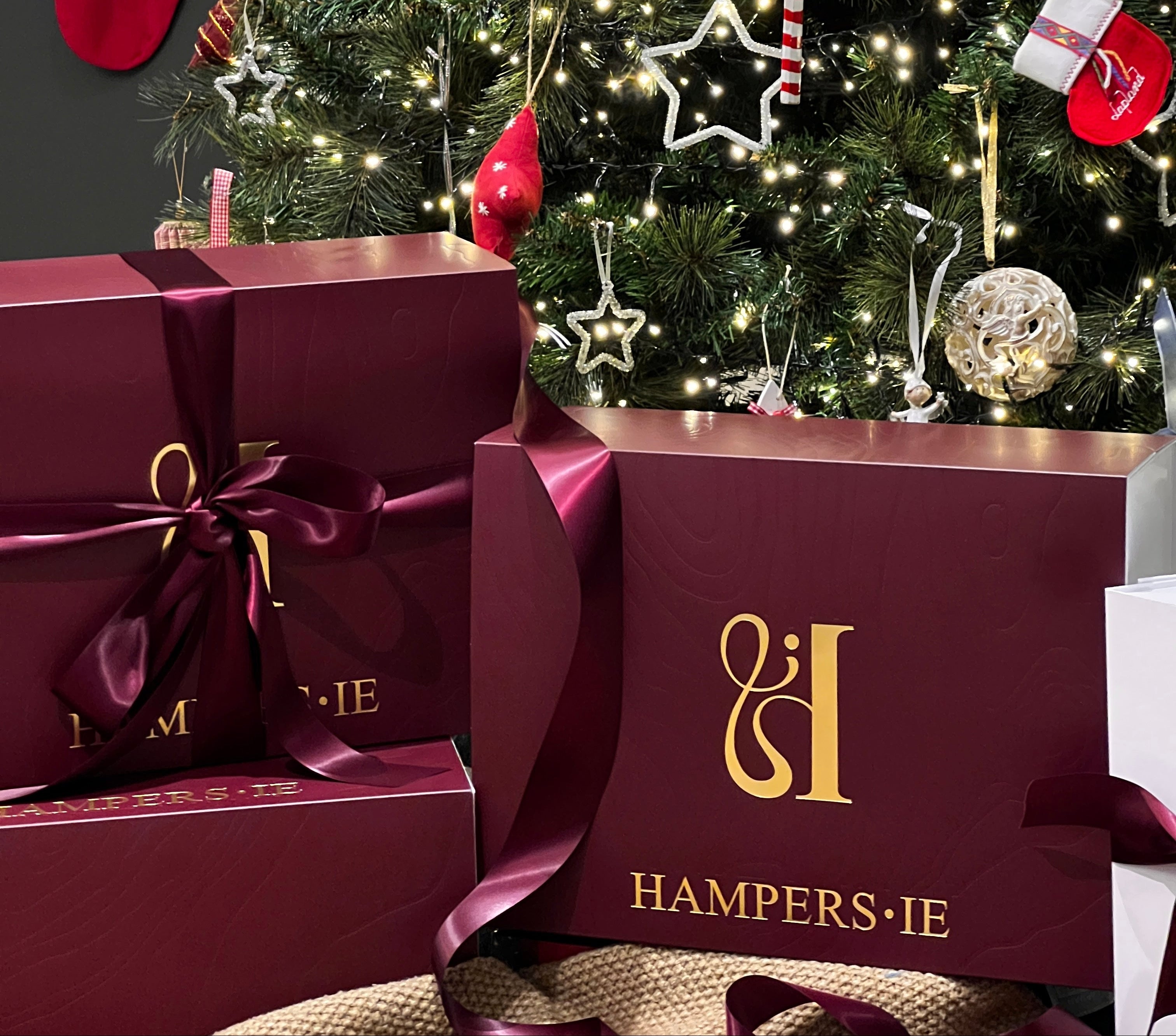 Decorated Christmas tree with ornaments and burgundy gift boxes featuring Hampers.ie branding.
