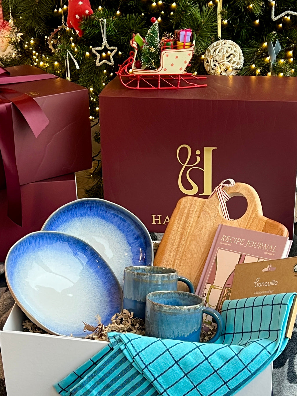 Gift set with blue ceramic plates, mugs, and wooden cutting board against a festive background.